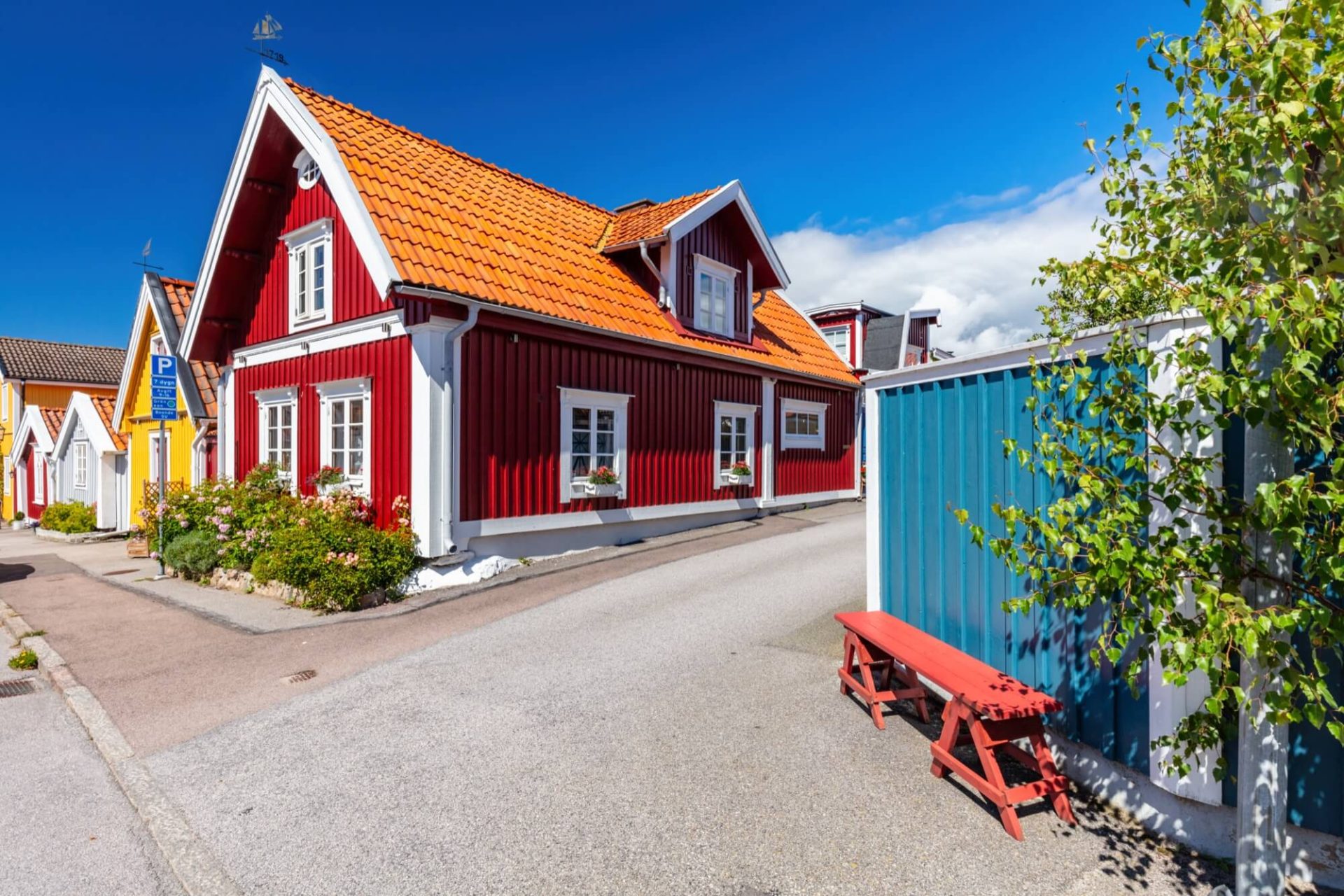 Ett charmigt rött trähus med vita knutar och ett tegeltak i orange, placerat mitt i en skärgårdsdröm